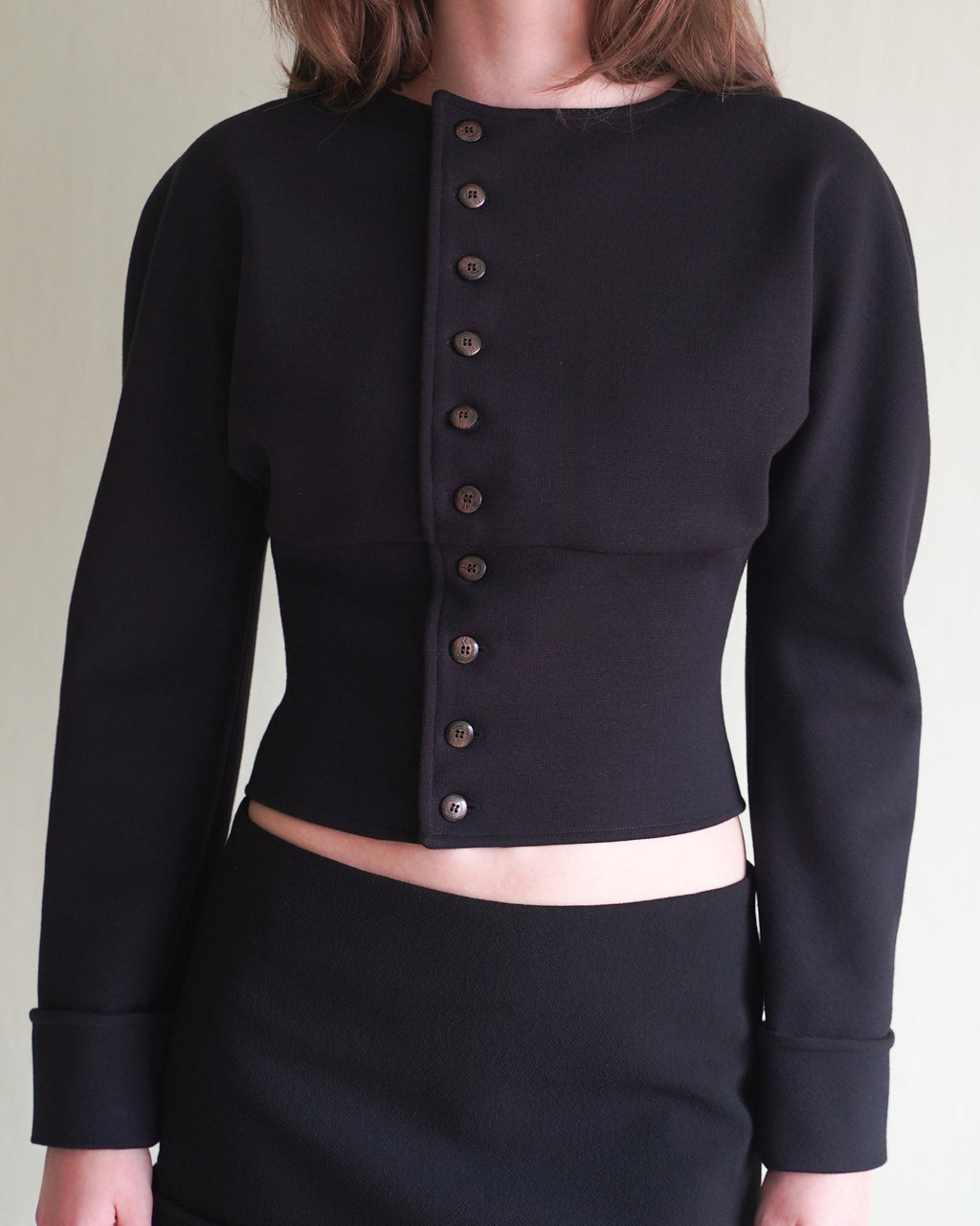 Woman wearing a black long-sleeve cardigan with coffee buttons and a black mini skirt against a plain background